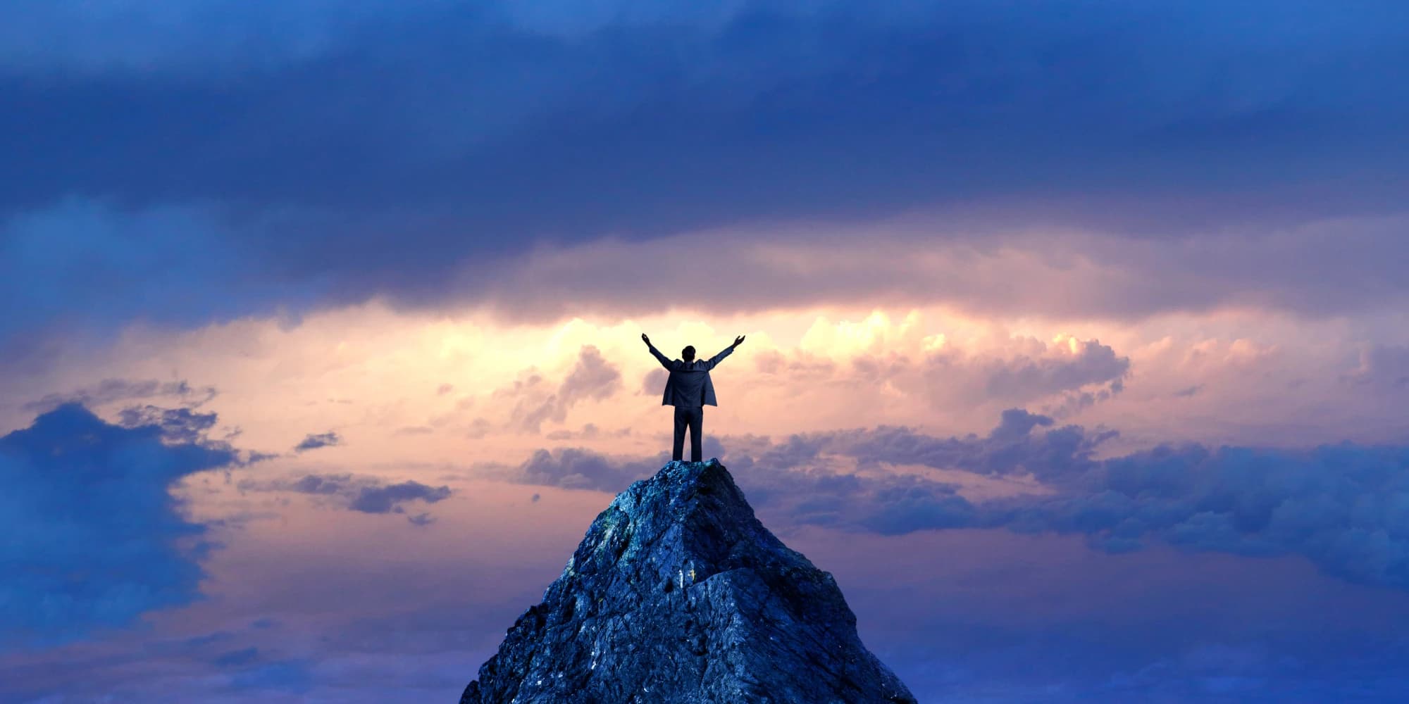 Person standing on a mountain peak with arms raised at sunset